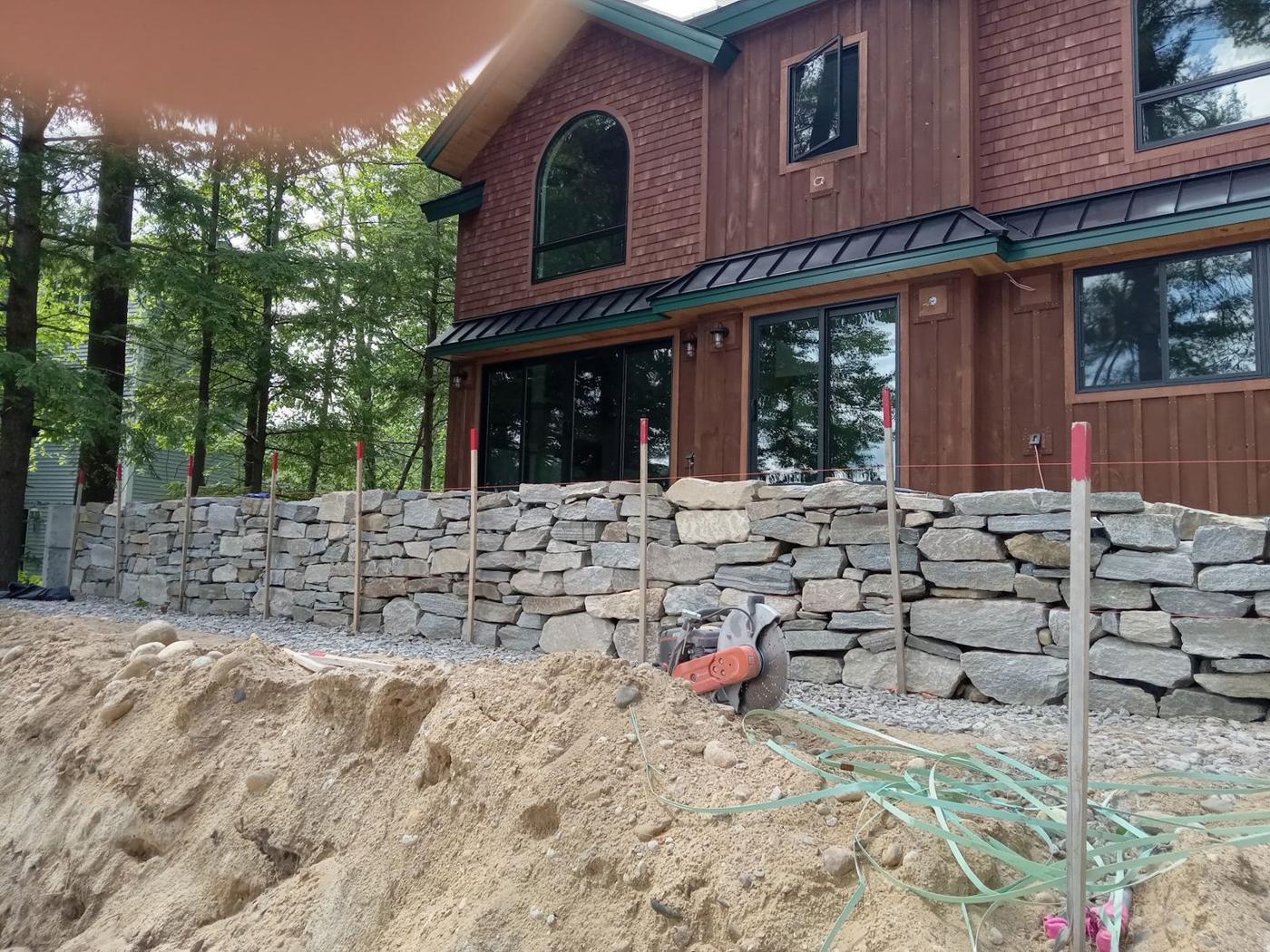 Fieldstone retaining wall in front of a red house